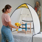 Person using a Wagner paint sprayer on a wooden chair inside a portable spray booth.
