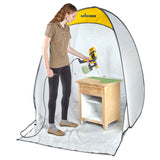 Person using a Wagner paint sprayer inside a portable spray booth to paint a wooden table.