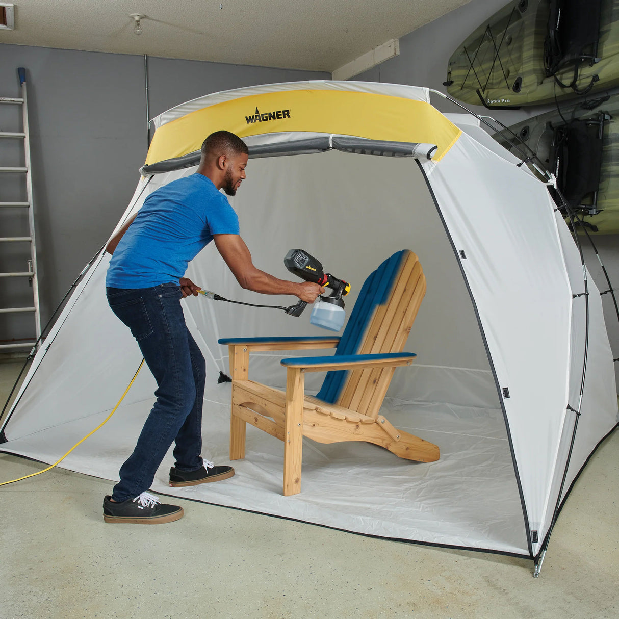 Person using a Wagner paint sprayer inside a portable spray booth to paint a wooden chair.