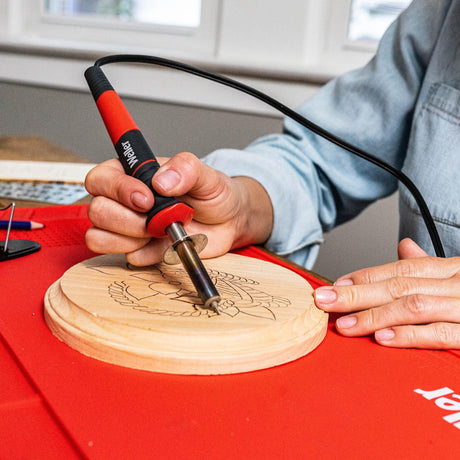 Person using a wood burning tool on a wooden disc with a design.
